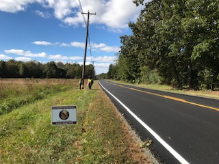 A view of a road with a grassy shoulder. In the grass, there is a South Jersey Quail Project sign.